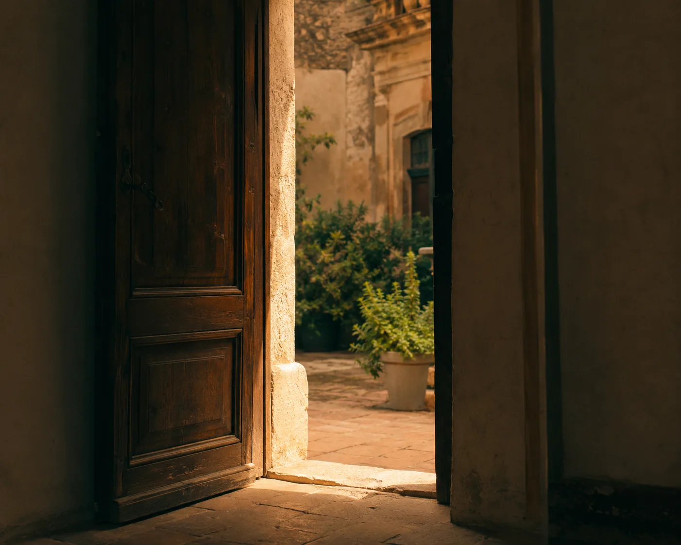 Una porta socchiusa su un cortile luminoso nel centro storico di Palermo, il calore di un'accoglienza di persona