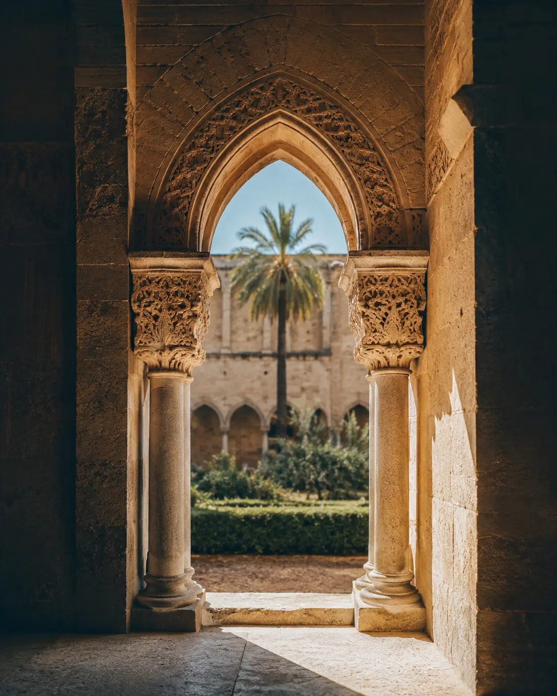 Un chiostro arabo-normanno a Palermo, colonne in pietra e un arco illuminato dal sole